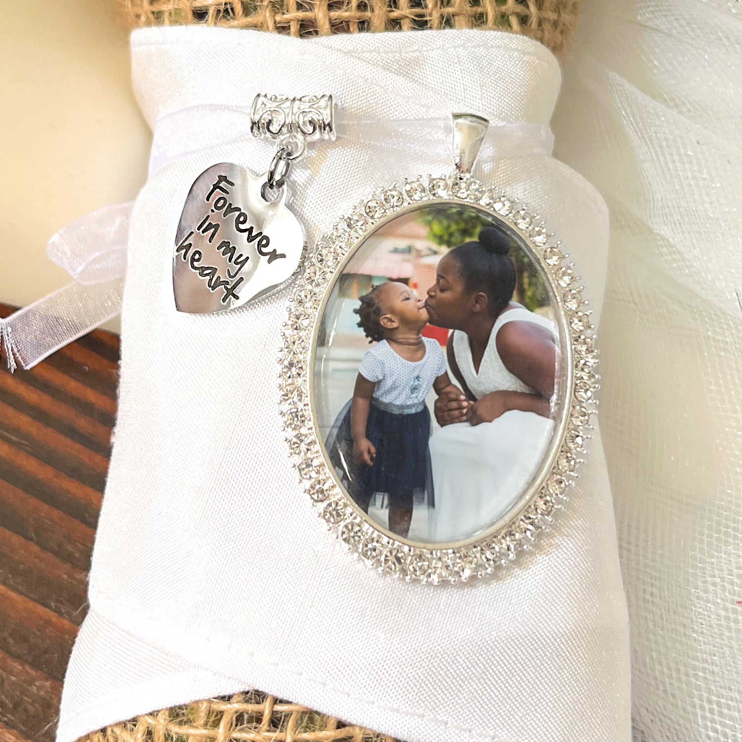 memorial photo charm in oval shape 30x40mm with rhinestones around the edge. Comes with saying charm: Forever in my heart. Attached to a white ribbon for bride to attach to bridal bouquet.