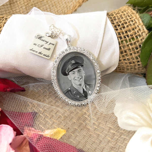 Bridal Memorial Photo Bouquet Charm in oval shape with clear rhinestones around edge of pendant. Image size is roughly 30mmx40mm. Comes with heart shape charm that reads, Missing you as I walk down the aisle. Pendant and charm come on a white ribbon to attach to bridal bouquet.