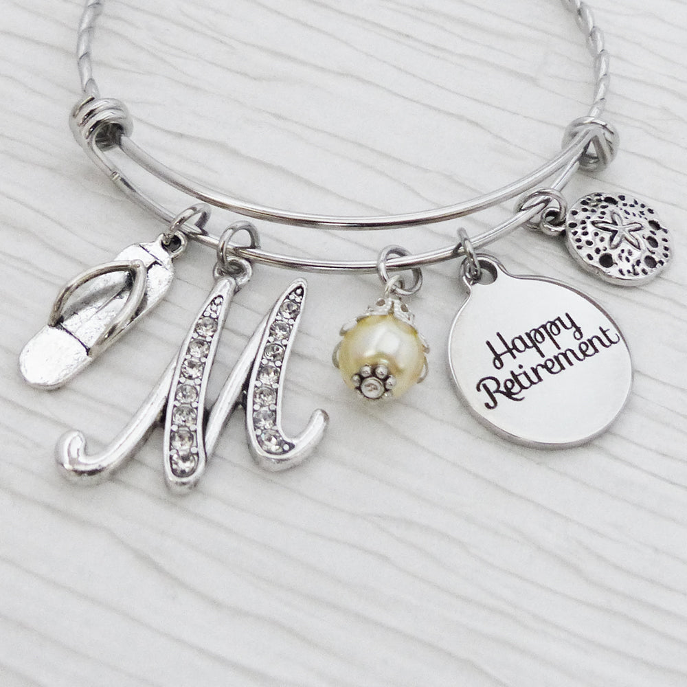 Personalized happy retirement bangle bracelet with rhinestone letter charm also includes a flip flop charm and a sand dollar charm and a cream bead